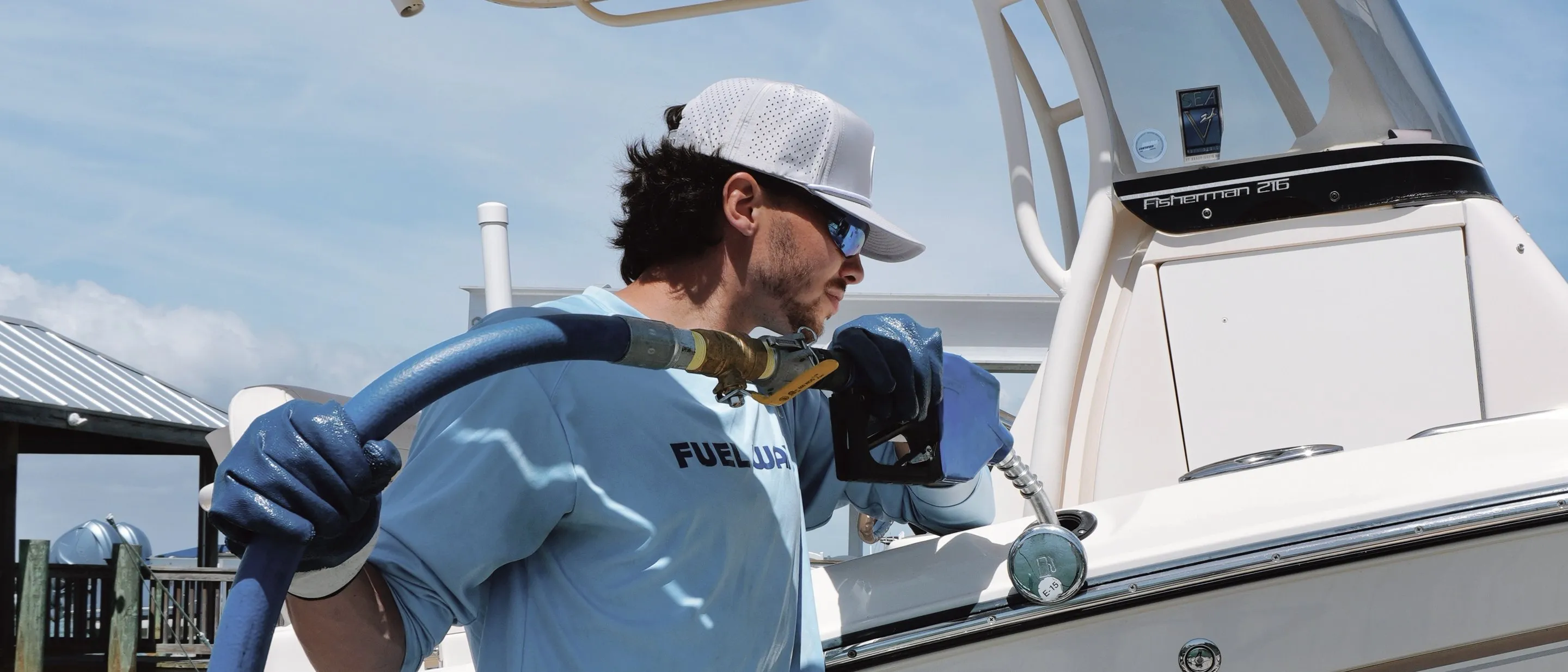 A Fuel Wave crew member with the hose over his shoulder, putting the nozzle into a boat's fuel port at the dock